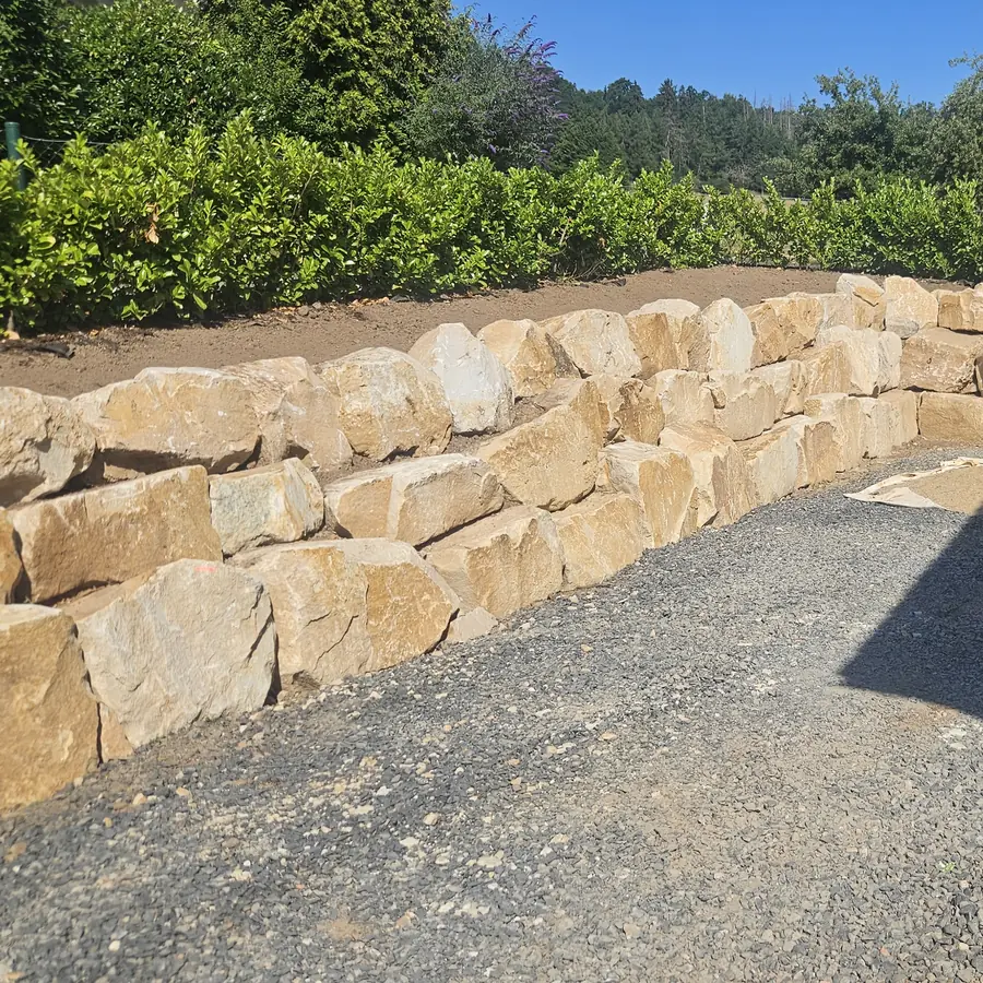 Natursteinmauer aus hellen Blöcken mit Hecke darüber