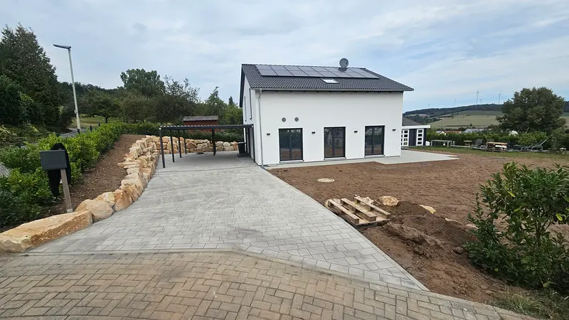 Gepflasterte Einfahrt mit Natursteinmauer, Carport und Neubau