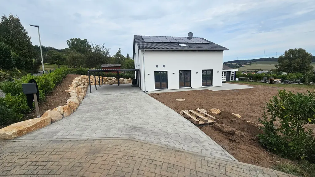 Neubau mit gepflasterter Einfahrt, Carport und Mauer aus Natursteinblöcken