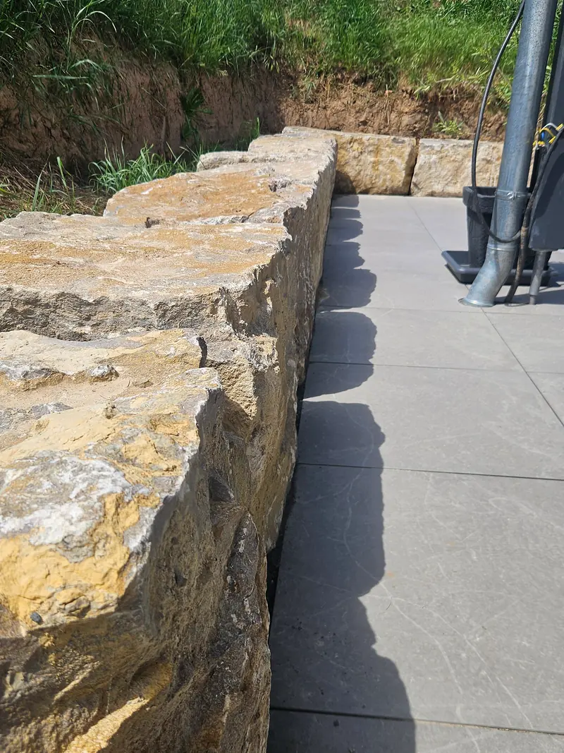 Mauer aus Natursteinblöcken an einer Terrasse aus großen Platten