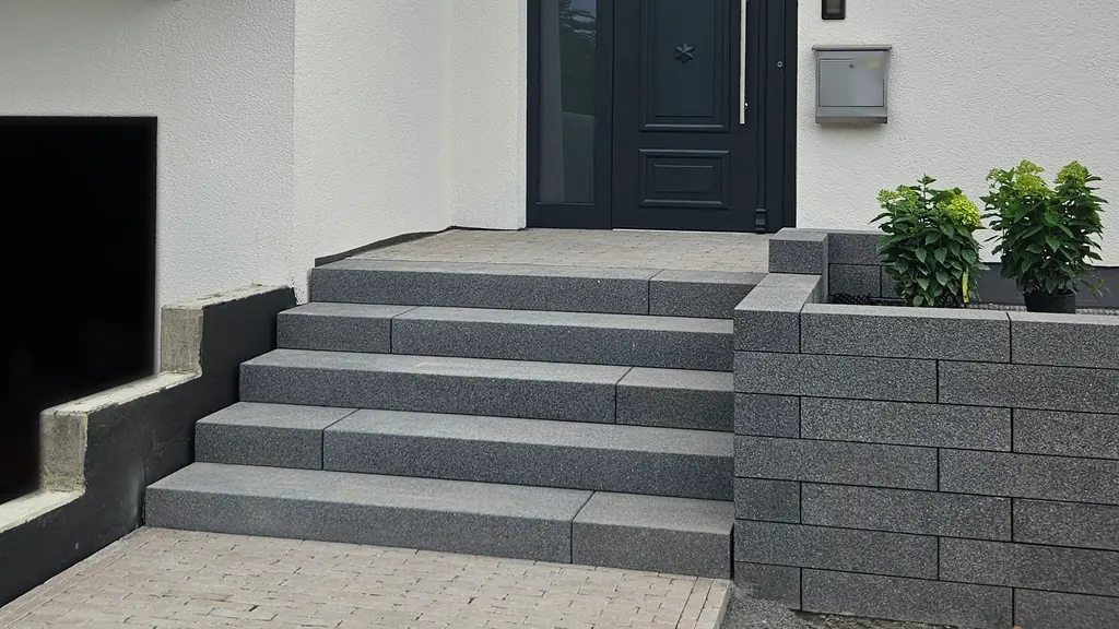 Außentreppe aus dunkelgrauen Blockstufen zur Haustür, rechts eine Mauer aus Mauersteinen