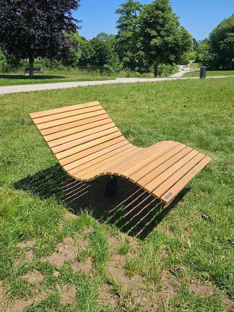 Geschwungene Liege aus Holz auf einer Wiese im Park