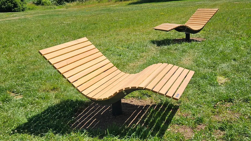 Zwei geschwungene Liegen aus Holz auf einer Wiese im Park
