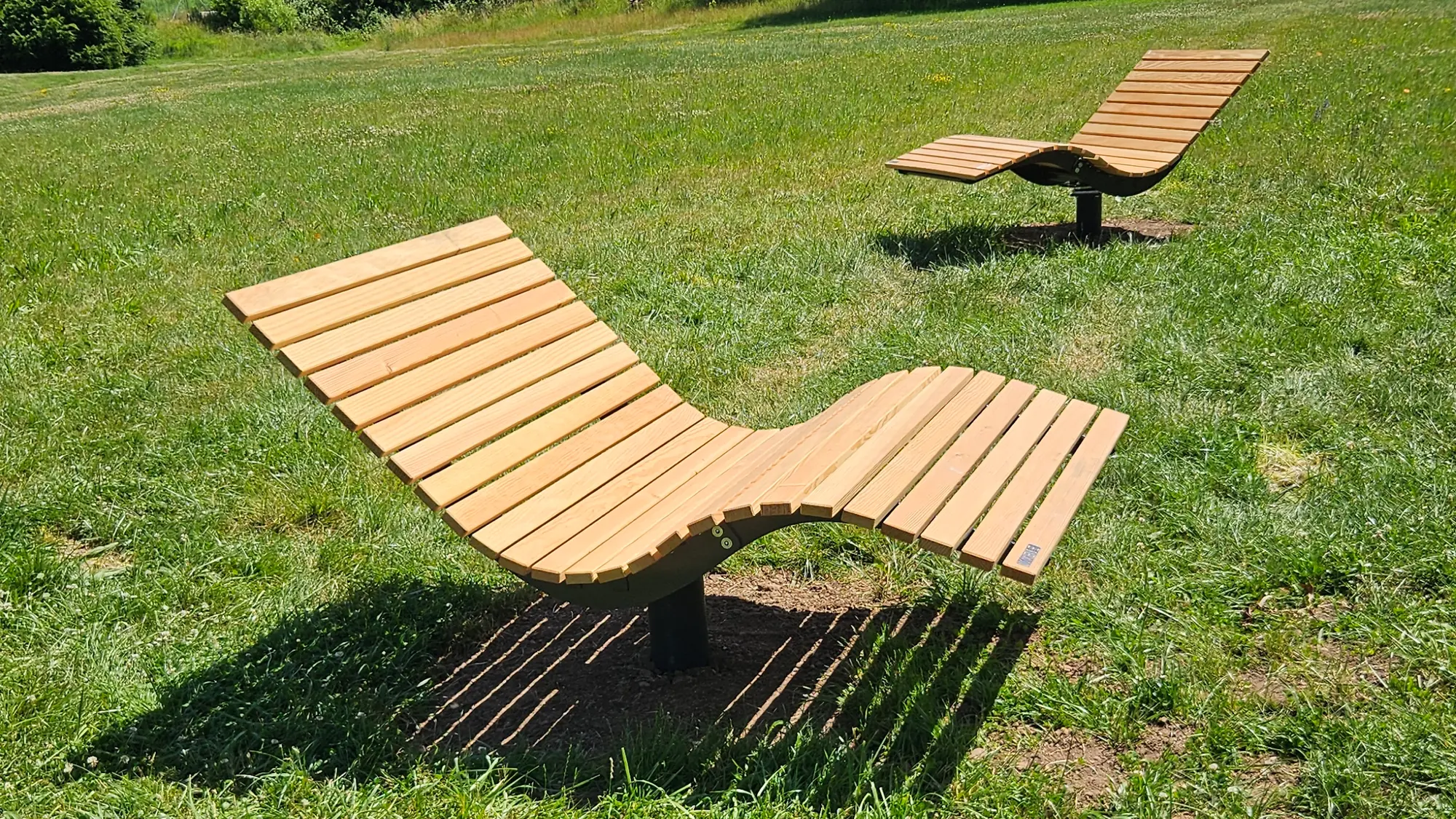 Zwei geschwungene Liegen aus Holz auf einer Wiese im Park