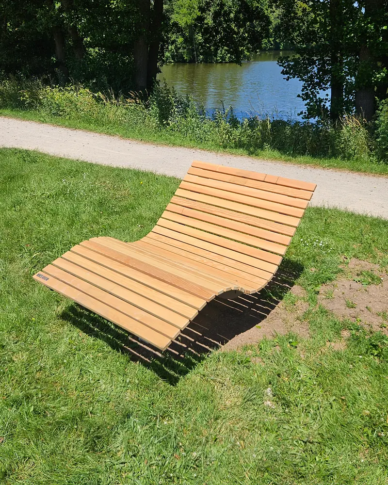 Zwei geschwungene Liegen aus Holz auf einer Wiese im Park