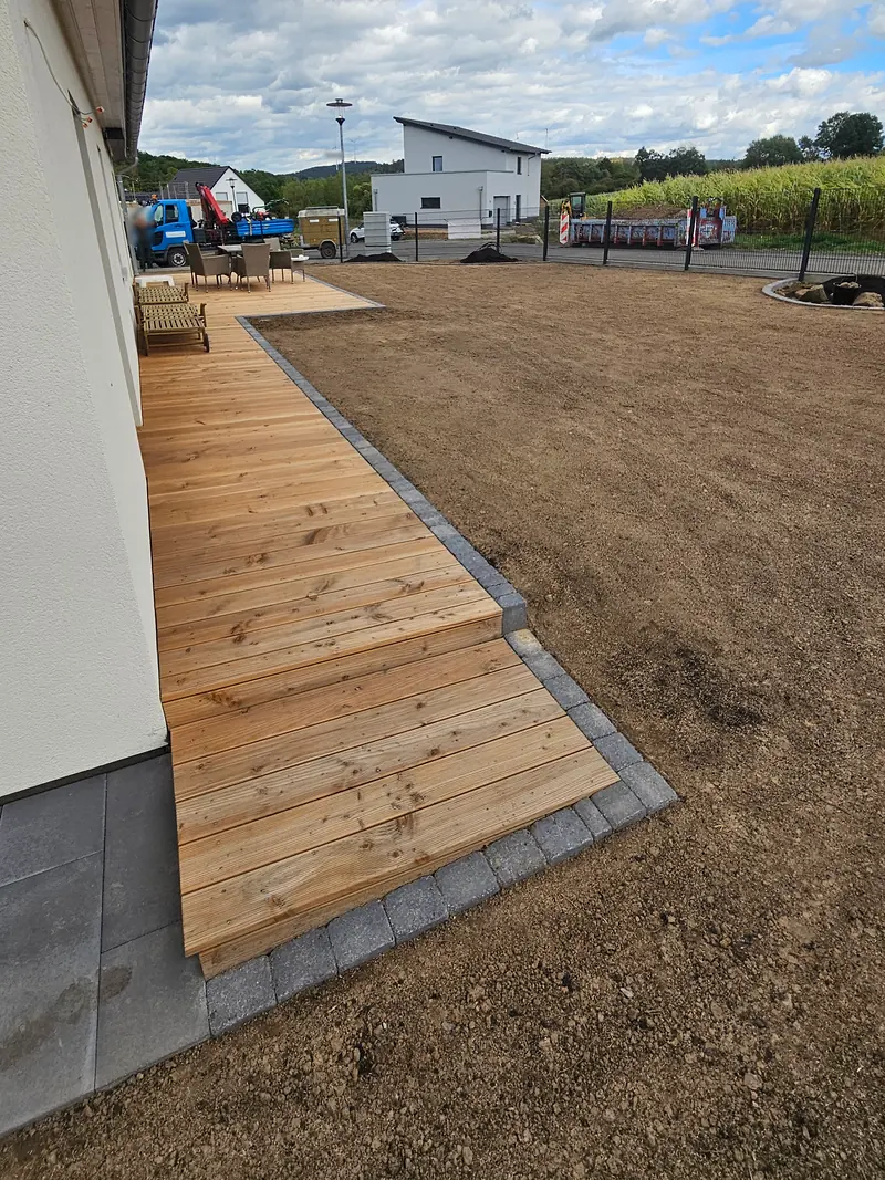 Steg aus Holzdielen entlang der Hauswand mit Einfassung aus Pflastersteinen