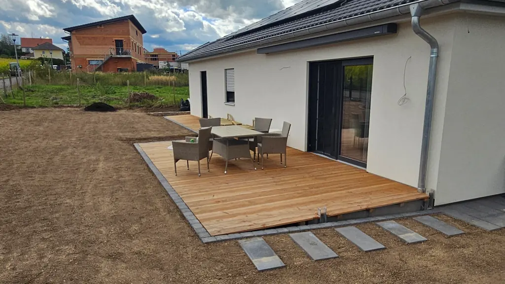 Holzterrasse mit Sitzgruppe an einem Bungalow, davor Trittplatten