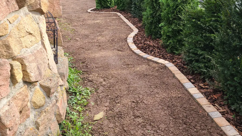 Geschwungene Rasenkante aus Pflastersteinen entlang einer jungen Hecke