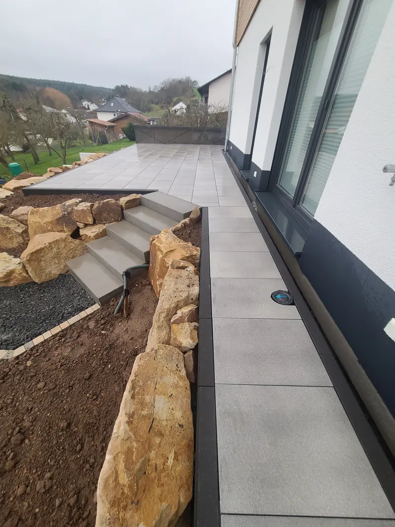 Weg aus großen Platten entlang der Hauswand, links die Treppe
