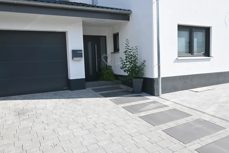 Einfahrt aus hellem Pflaster mit dunklen Trittplatten zur Haustür