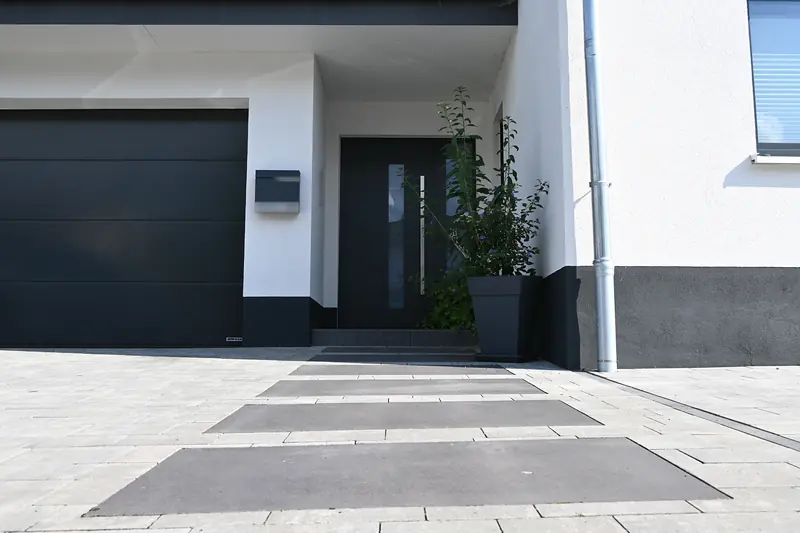 Dunkle Trittplatten im hellen Pflaster vor Haustür und Garage