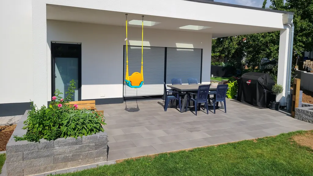 Überdachte Terrasse aus großen Platten mit Hochbeet aus Mauersteinen