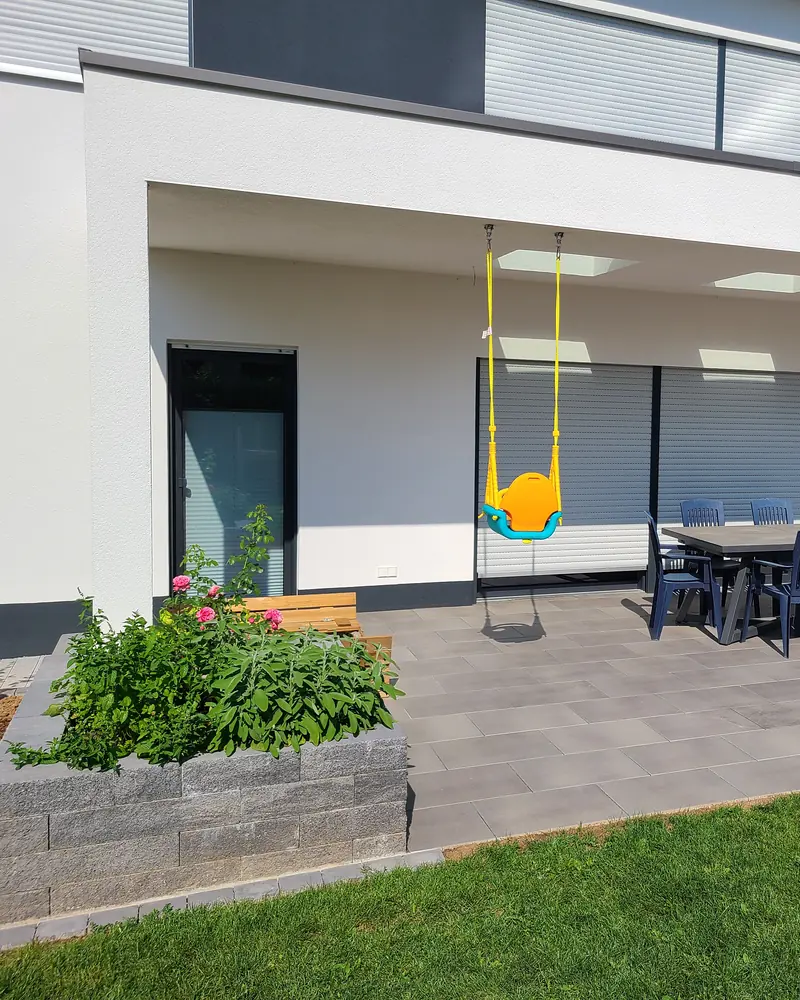 Überdachte Terrasse aus großen Platten mit Hochbeet aus Mauersteinen