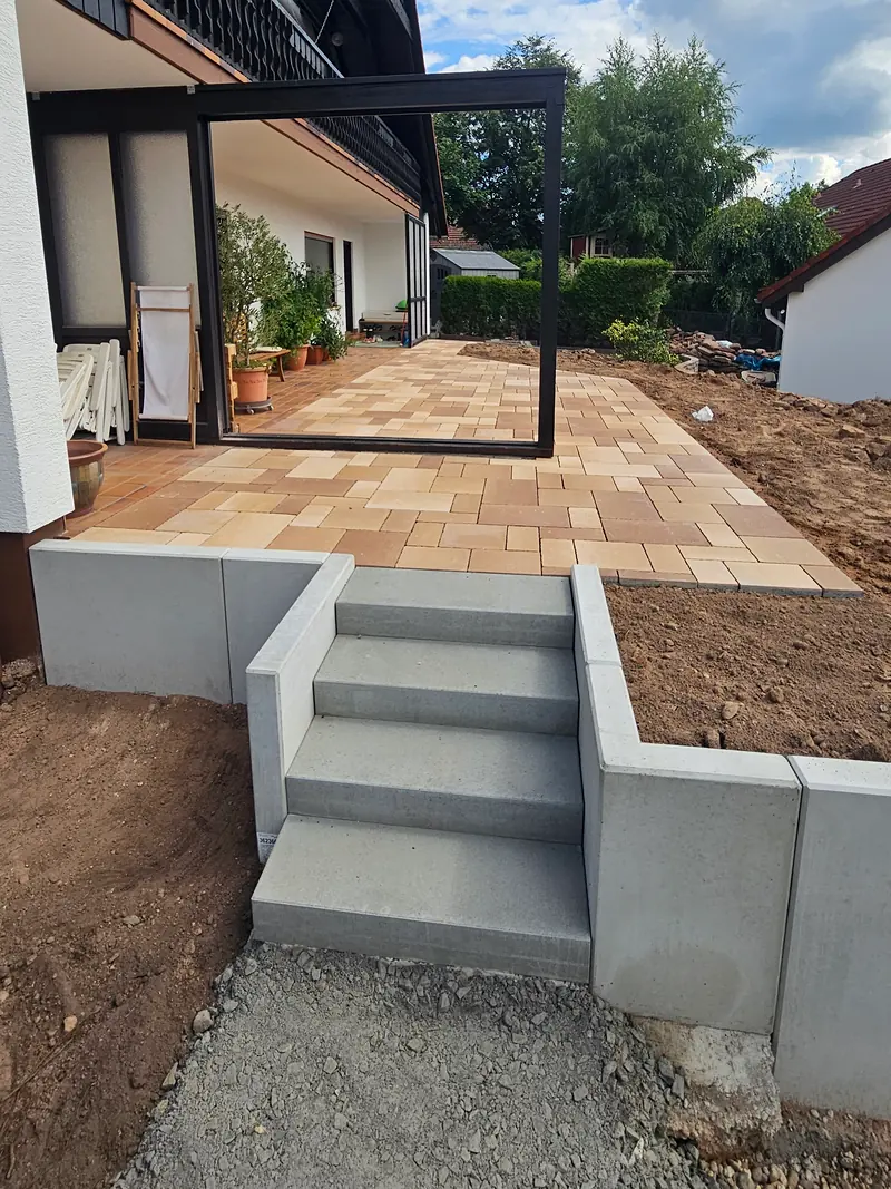 Treppe aus grauen Blockstufen mit Winkelsteinen, oben die Terrasse