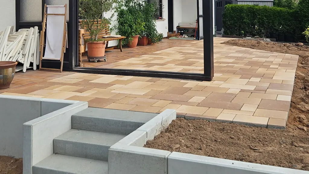 Terrasse aus Pflaster in warmen Farbtönen mit Treppe aus Blockstufen und Winkelsteinen