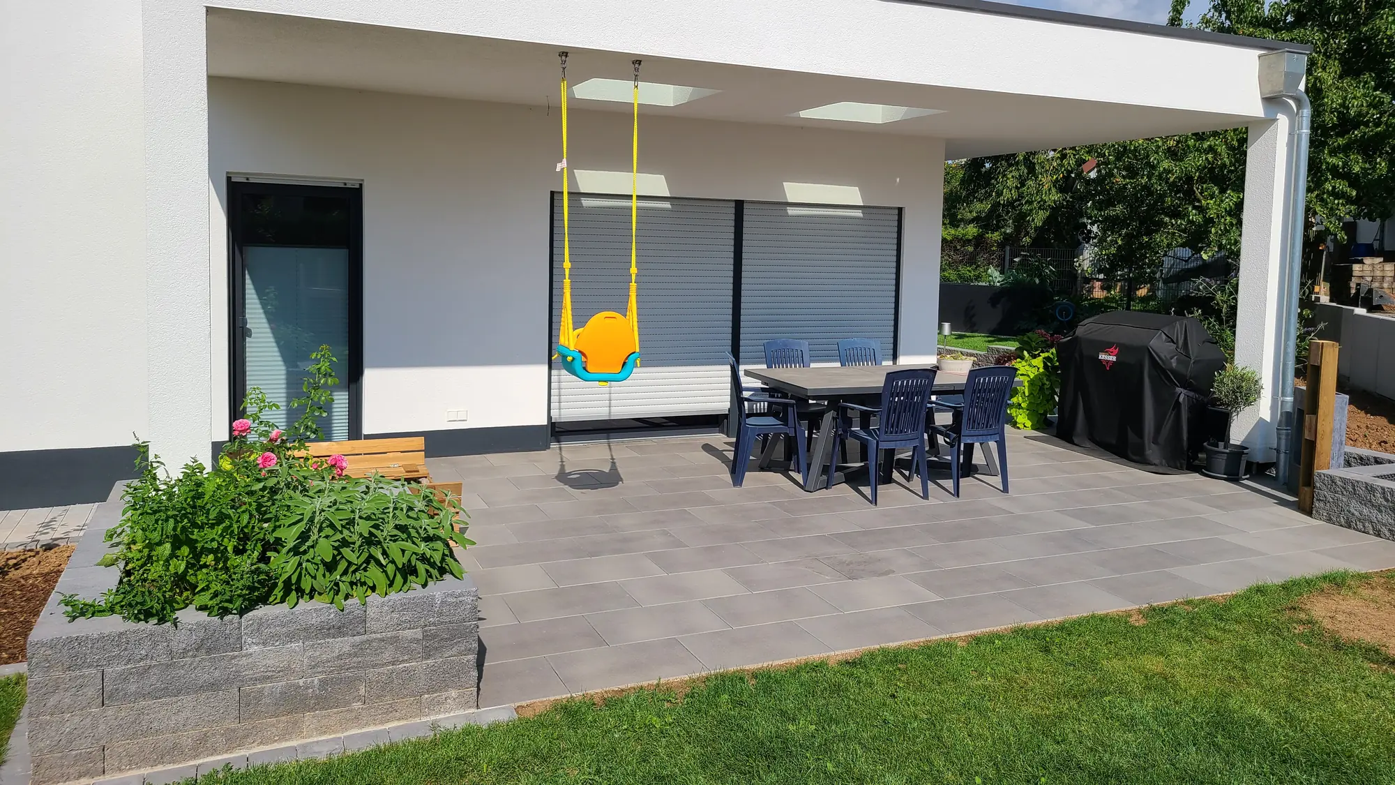 Überdachte Terrasse mit Großformatplatten, Esstisch und Hochbeet